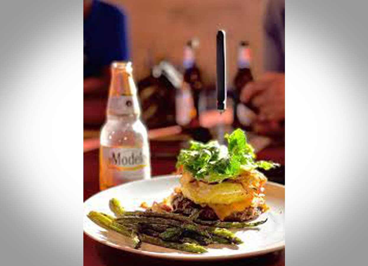 Showing a burger served with asparagus and a Modello beer.
